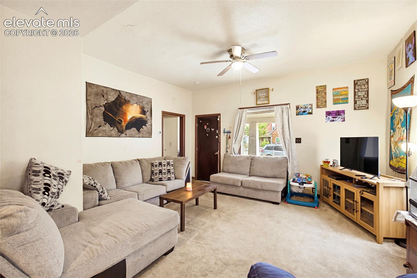 Textured carpeting throughout, a ceiling fan with integrated lighting, and a window with a valance
