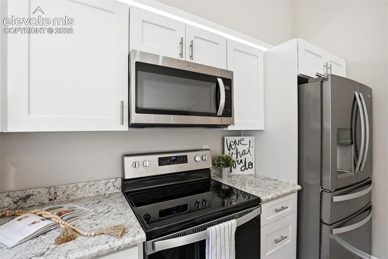 Modern kitchen featuring white flat-panel cabinetry, light granite countertops, and stainless steel appliances including an over-the-range microwave, electric range, and French door refrigerator