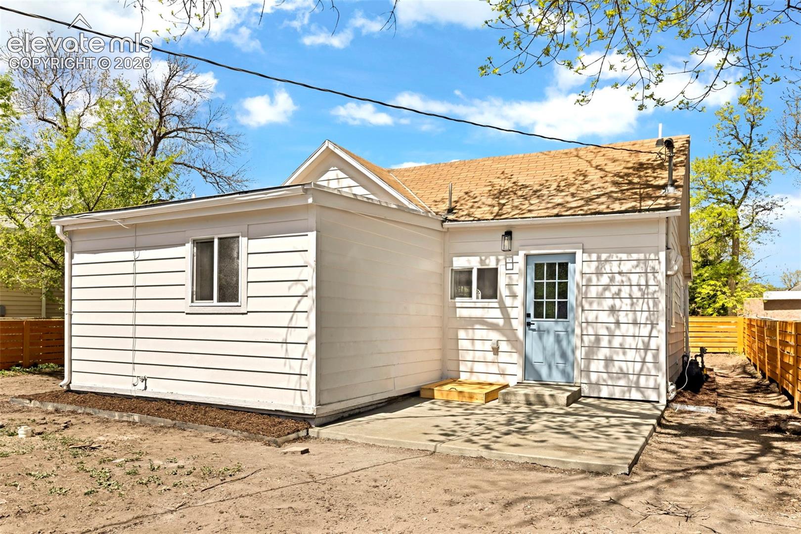 White horizontal siding exterior with a light blue entry door, concrete patio, and a brown shingle roof