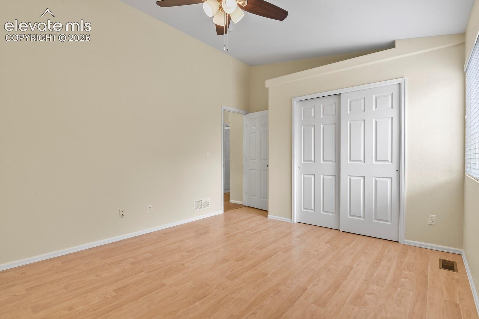Spacious room featuring vaulted ceilings, wood-finish flooring, a ceiling fan, and sliding panel closet doors