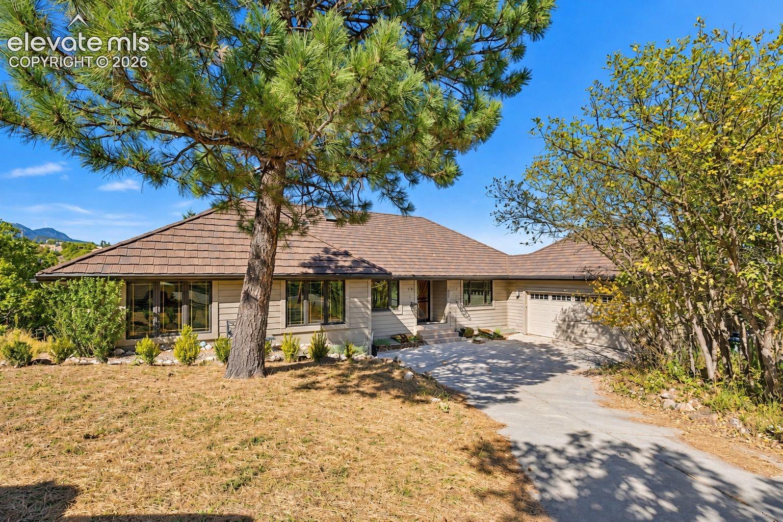 Single-story residence featuring horizontal siding, a multi-faceted hipped roof, a two-car attached garage, and mature pine trees