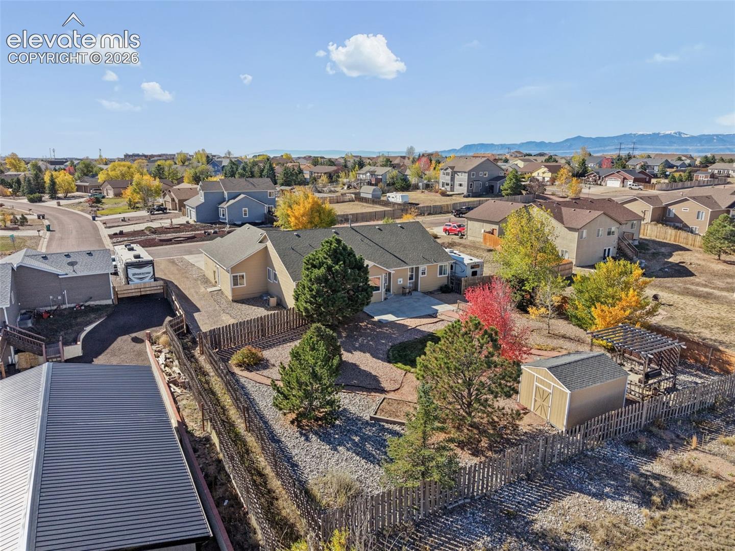 Aerial perspective of a property featuring a fenced backyard with xeriscaping, mature trees, a detached storage shed, a wooden pergola, and a concrete patio