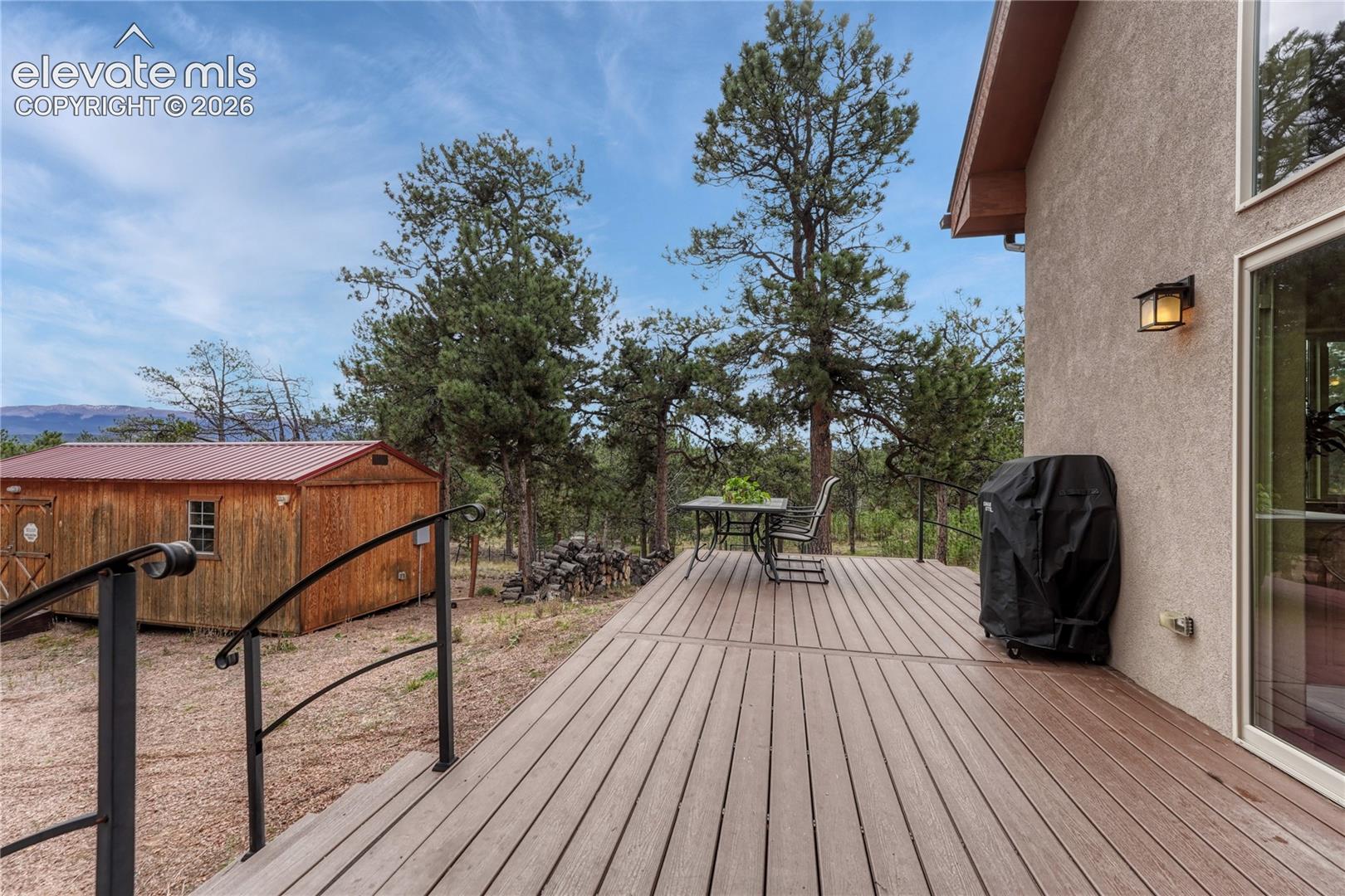 Composite decking with metal railings, stucco exterior finish, wall-mounted outdoor lighting