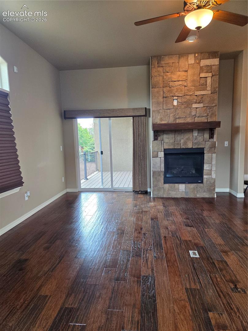 OPEN-Spacious interior featuring wide-plank wood flooring, a stone-clad fireplace with a wood mantle, a ceiling fan with integrated lighting, and direct access to an outdoor deck through sliding glass doors