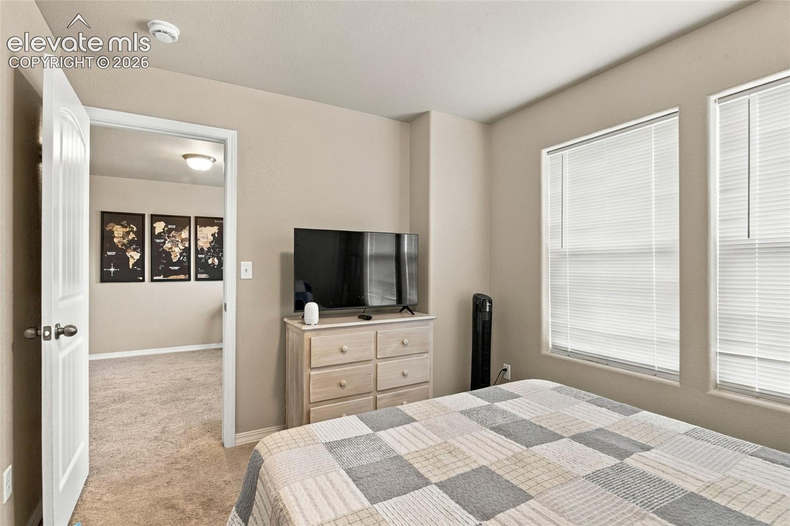 Room featuring neutral-toned walls, carpeting, dual windows with integrated blinds, and a paneled interior door