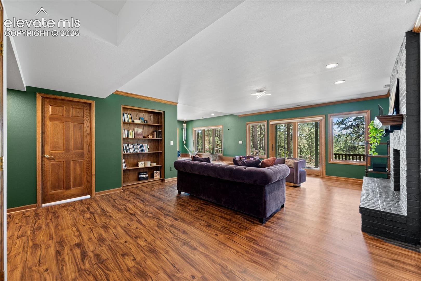 Spacious living area featuring wood-finish flooring, built-in shelving, and a dark brick fireplace with a wood mantel