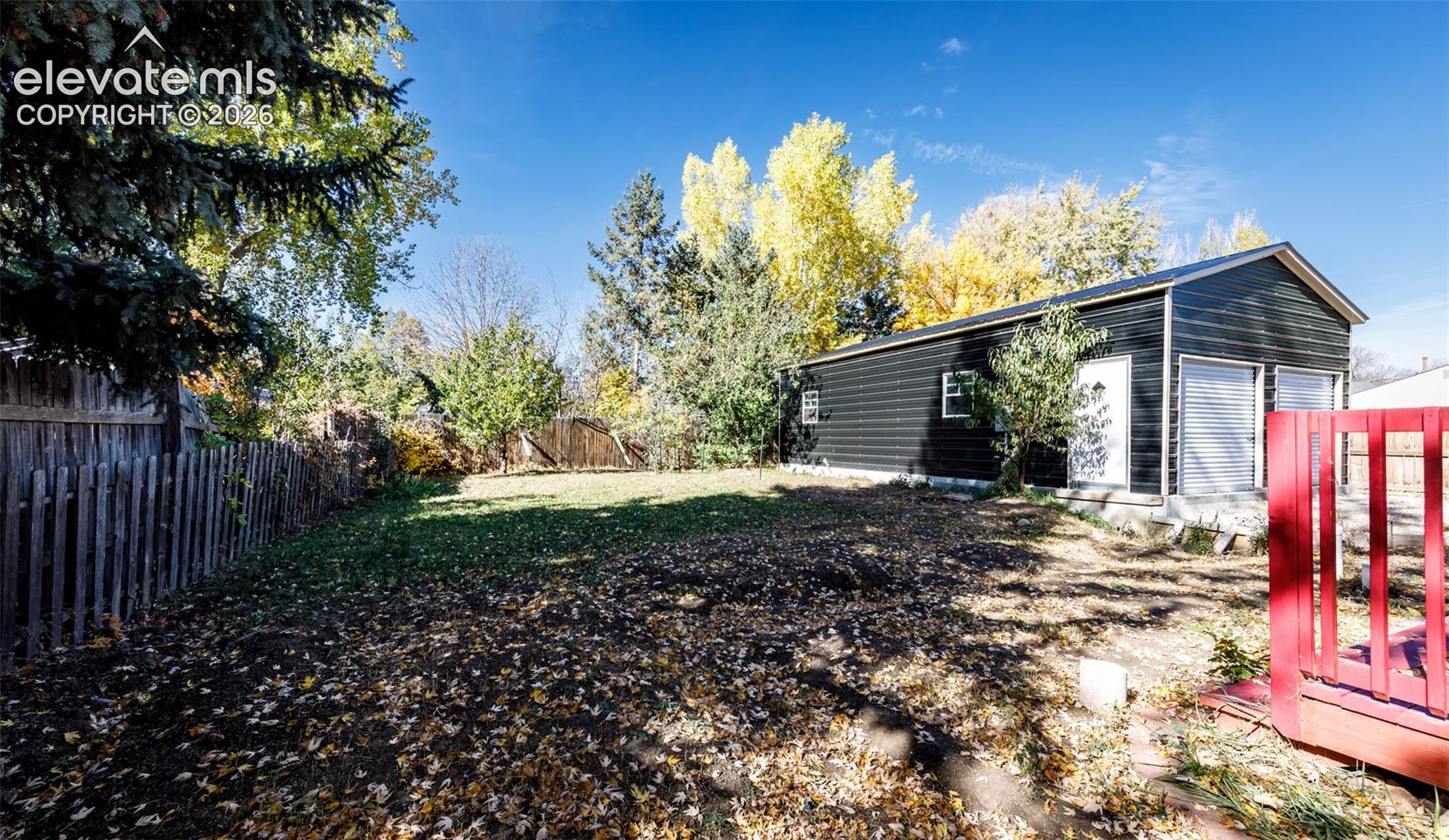 Backyard featuring a detached garage with dark horizontal siding, a red-painted wood deck, and wood perimeter fencing