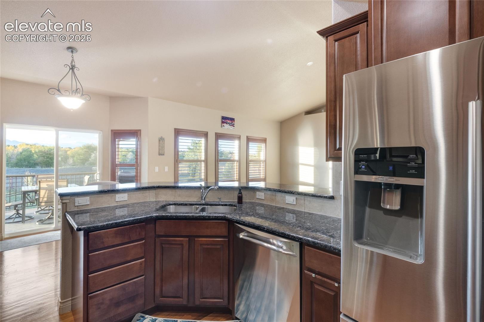 Kitchen featuring dark wood-finish cabinetry, stone countertops, stainless steel appliances, and a dual-basin undermount sink