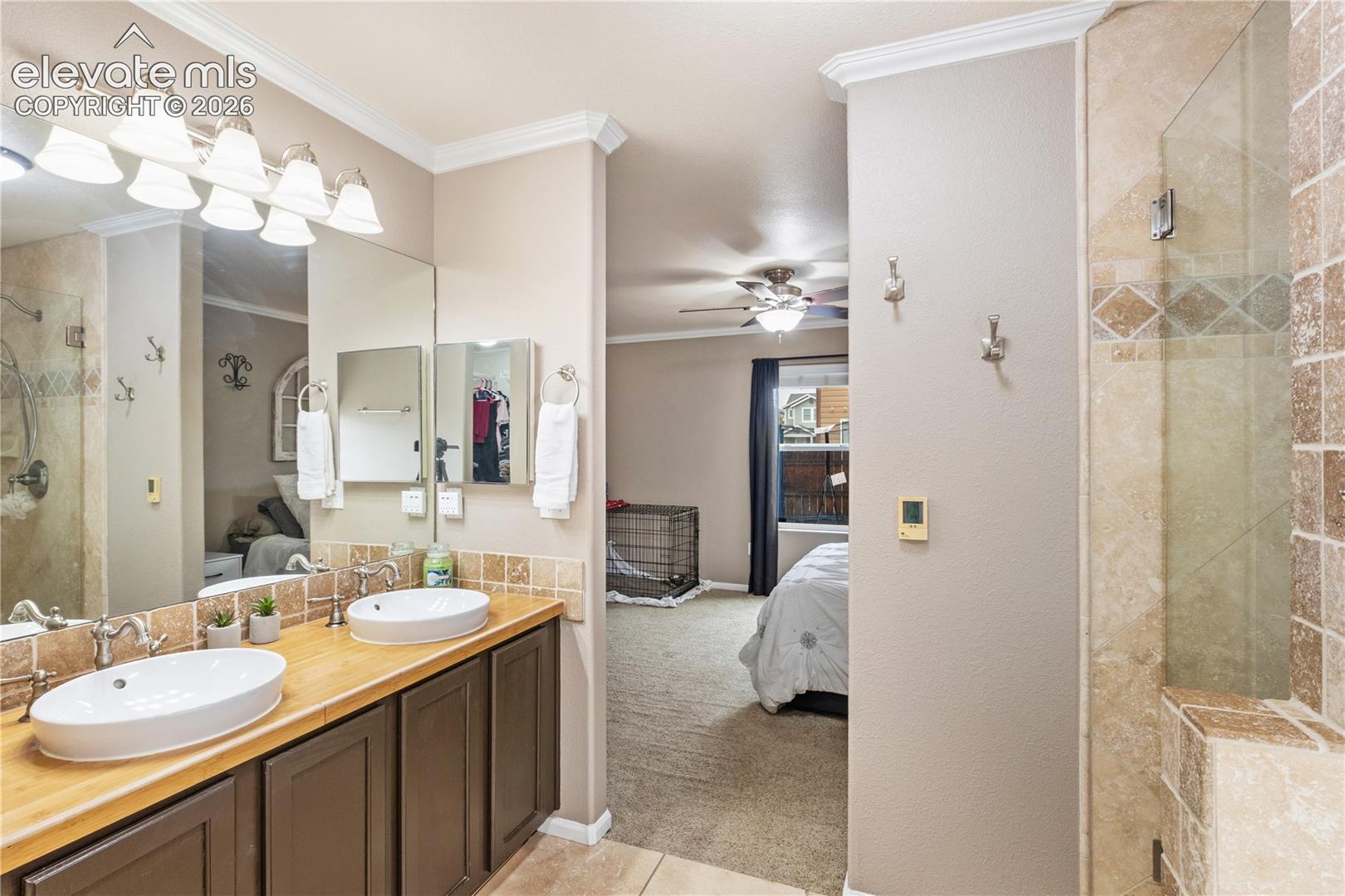 Bathroom featuring a dual-sink vanity with vessel sinks, wood-finish countertop, dark cabinetry, and a walk-in shower with tiled surround and glass enclosure
