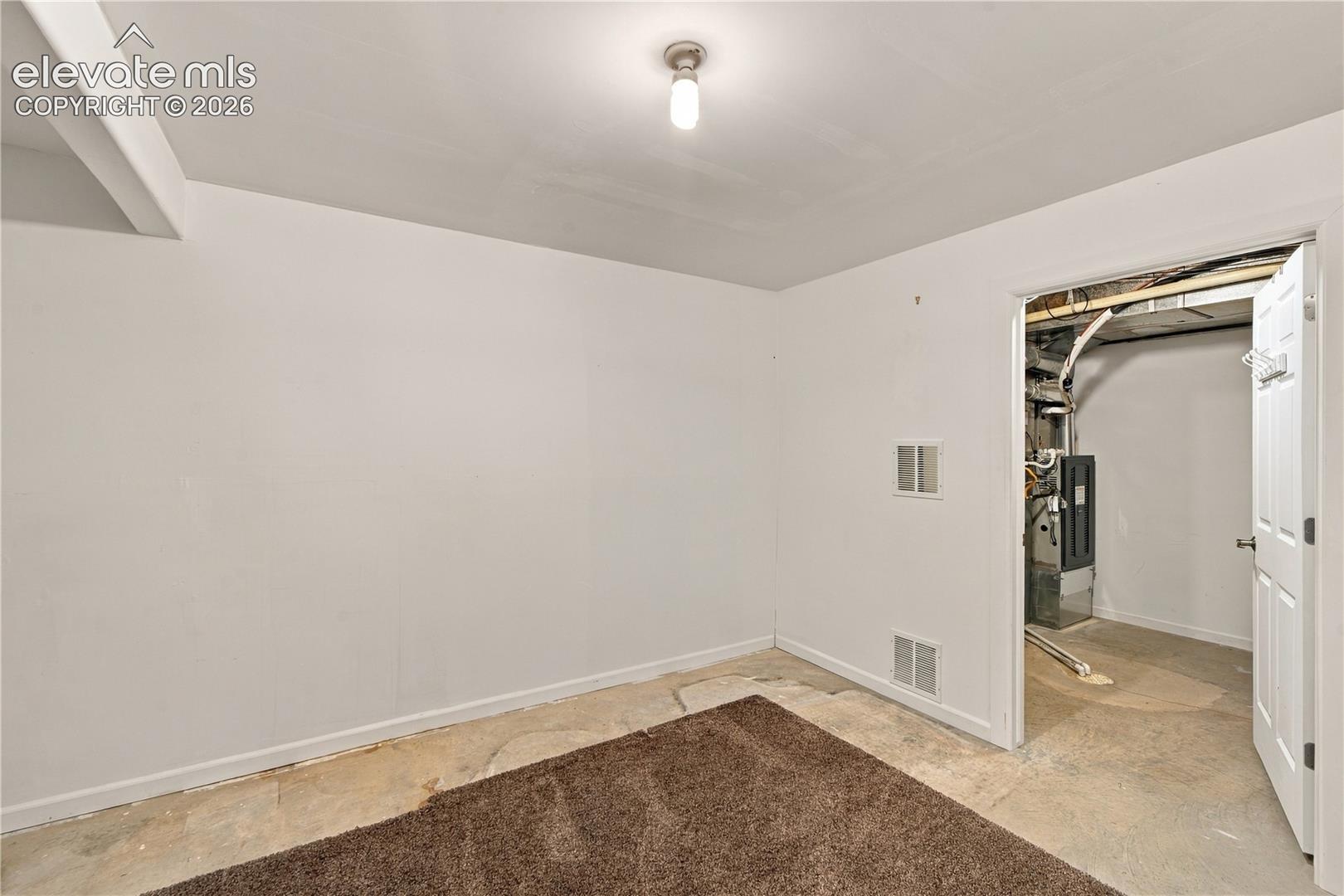 Interior space featuring white-painted walls, a single-bulb ceiling fixture, and a white interior door opening to a mechanical utility area