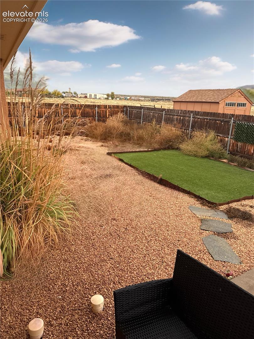 Backyard featuring synthetic turf, decorative gravel ground cover, natural stone paver pathway, wood perimeter fencing, and a detached storage shed