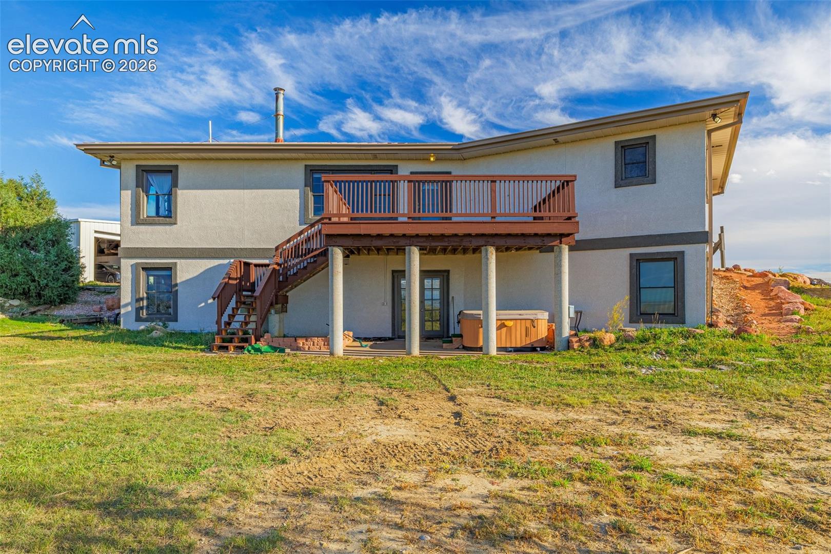Rear elevation with a multi-level deck featuring wood railings, a lower-level concrete patio, and stucco exterior finish