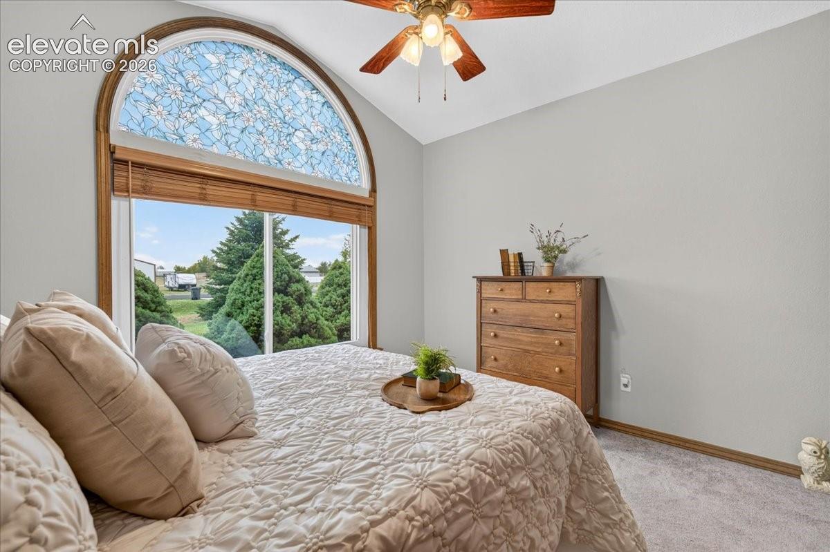 Vaulted ceiling featuring an arched window with decorative leaded glass, neutral wall tones, and a multi-blade ceiling fan with integrated lighting