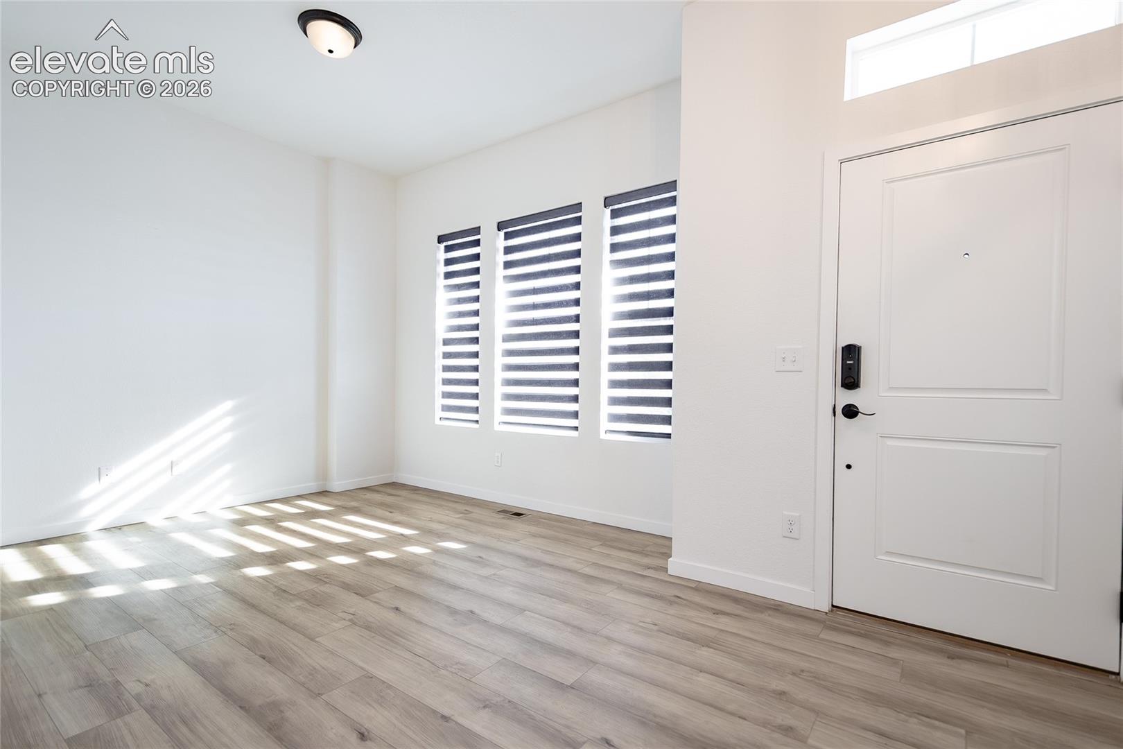 Entry area featuring wood-finish flooring, high ceilings with a transom window, three tall windows with integrated blinds, and a paneled entry door with an electronic lockset