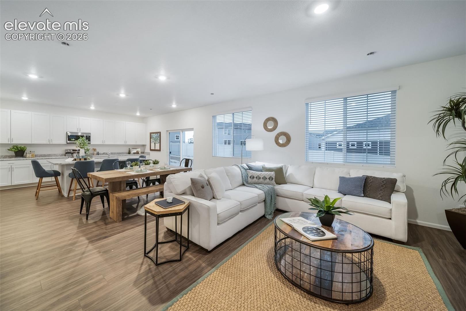 Open-concept living space featuring wood-finish flooring, recessed lighting, white cabinetry, a kitchen island with seating, and stainless steel appliances
*photos of a model home*