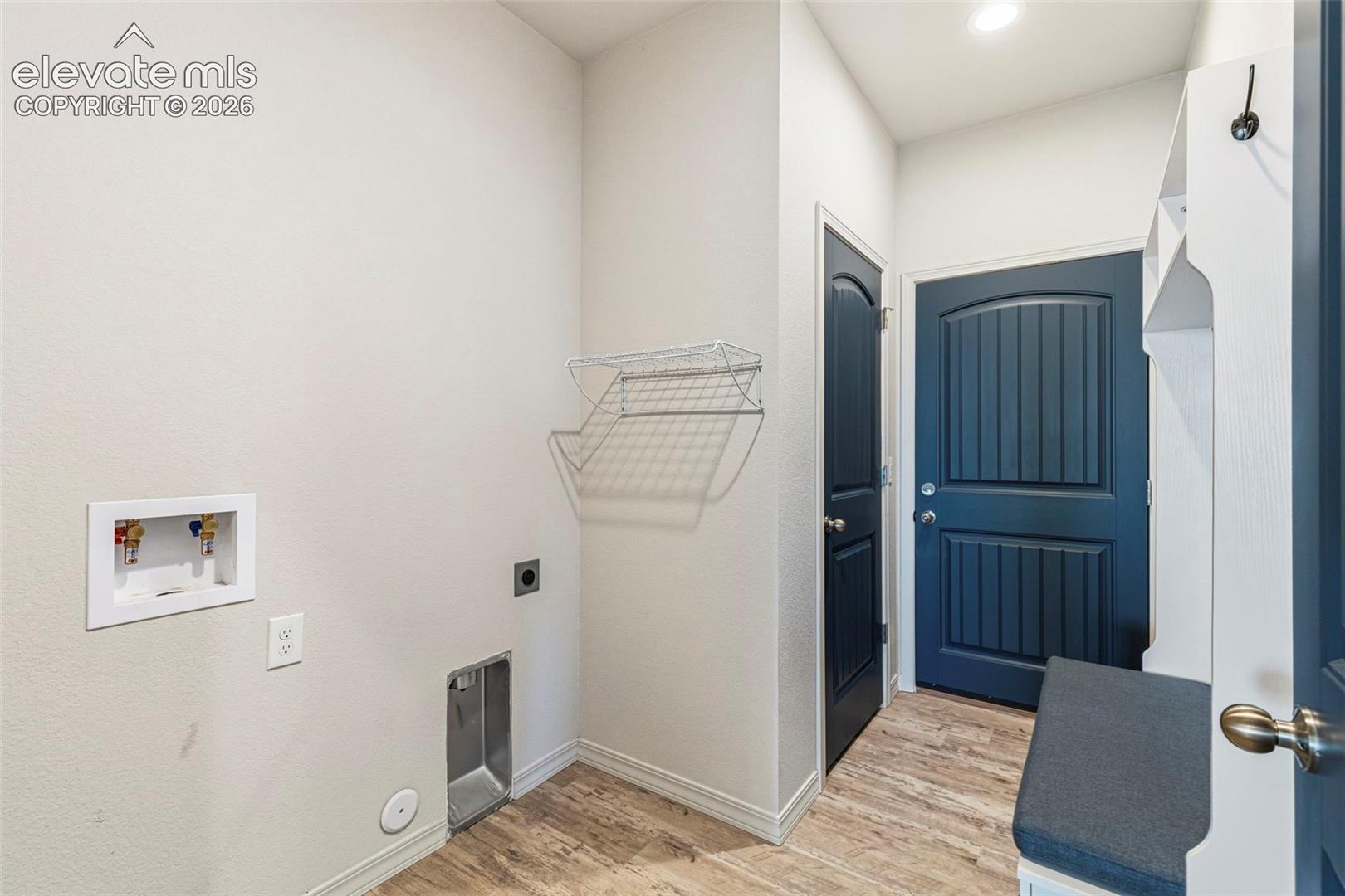 Functional utility room featuring wood-finish flooring, laundry hookups, and a built-in wire shelving unit