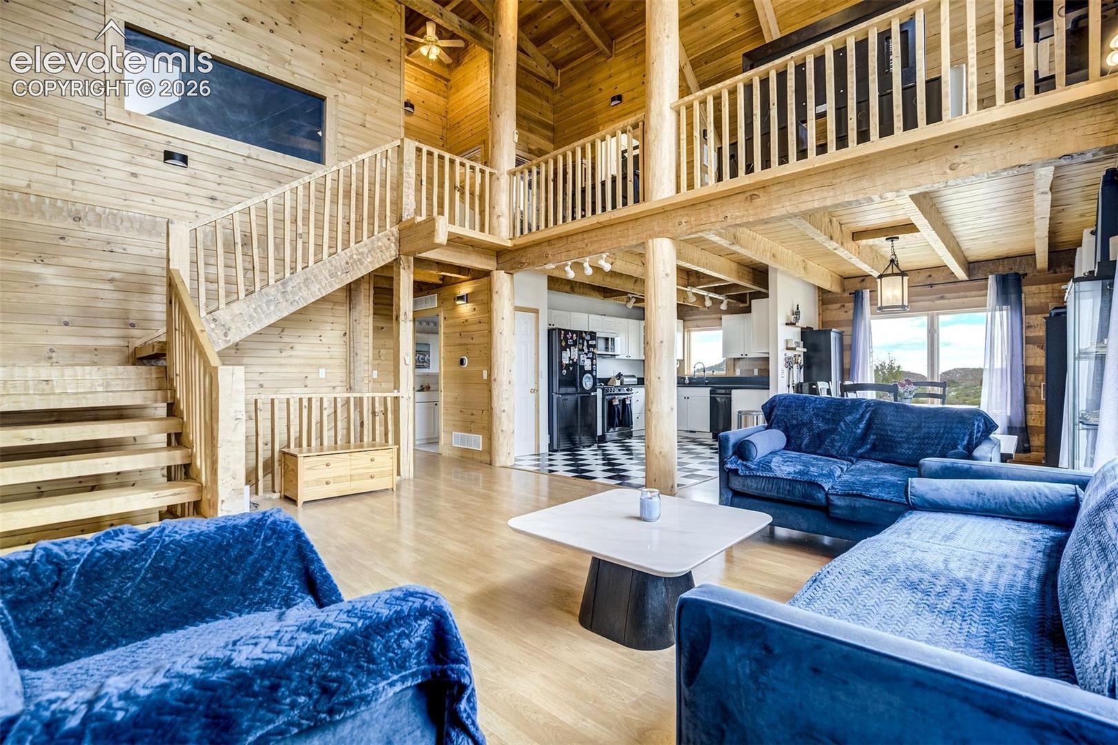 Expansive open-concept living space featuring wood-finish flooring, exposed wooden beams, a prominent staircase, and a lofted area with wood railings