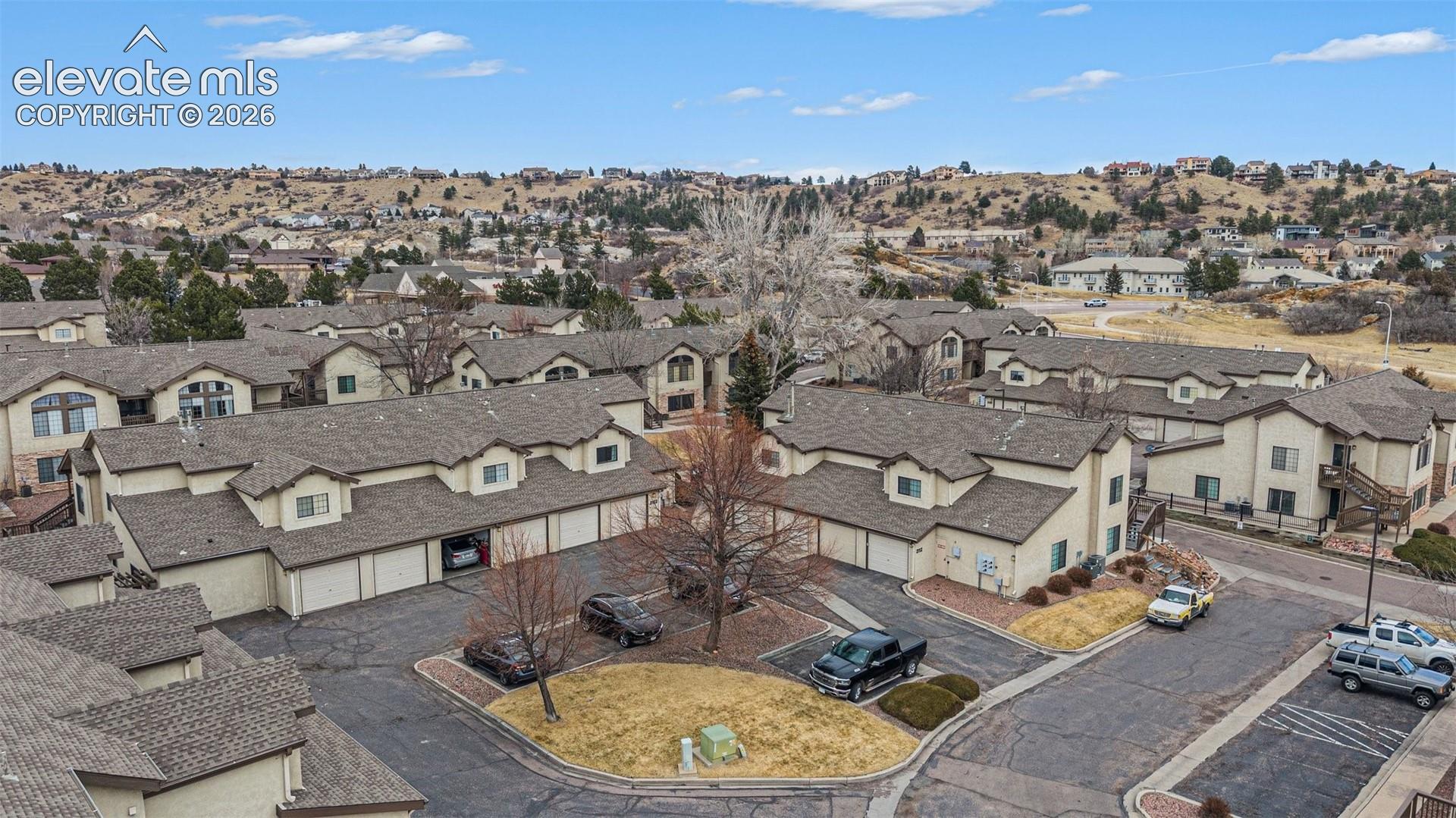 Aerial perspective of multi-family complex featuring multi-gabled roofs, integrated garage spaces, paved parking areas, and mature landscaping