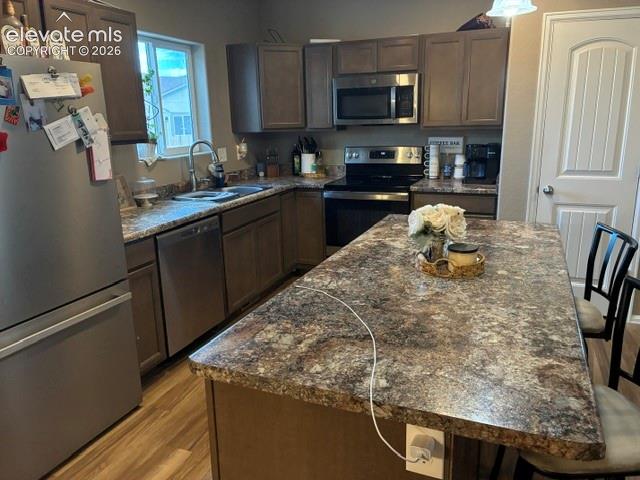 Kitchen featuring cabinetry with a dark finish, integrated stainless steel appliances, a center island with a stone-patterned countertop, and wood-finish flooring