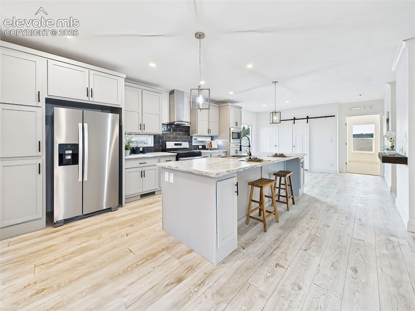 Modern kitchen with stainless steel appliances, shaker cabinetry, sliding barn door pantry, and durable luxury vinyl flooring extending to the entryway.