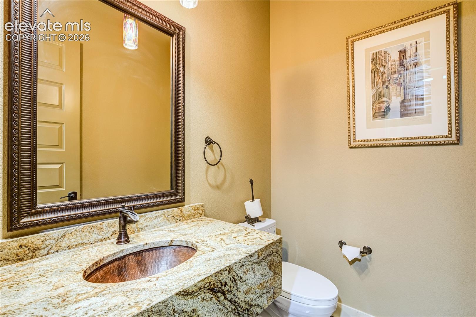 Refined finishes extend to the main-level powder bath, where a granite-topped vanity, decorative mirror + warm architectural details create an inviting space for guests.