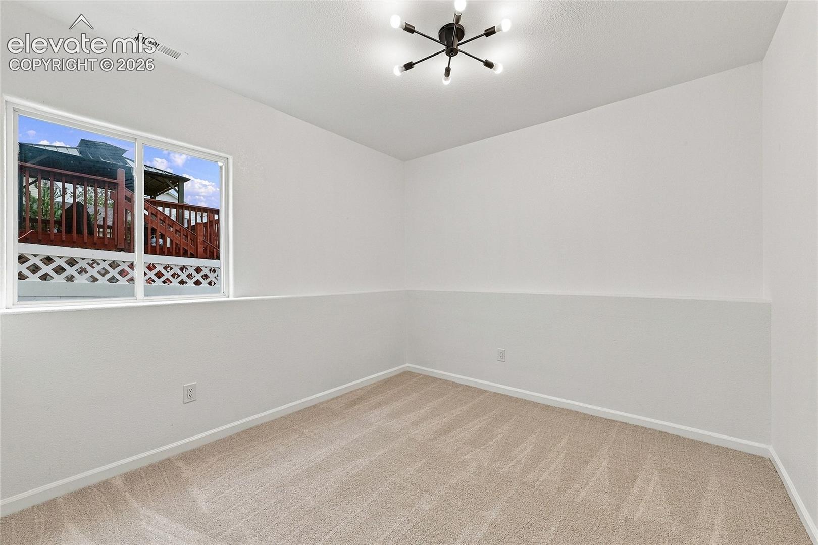 Neutral interior featuring wall-to-wall carpeting, a multi-arm modern light fixture, and a large window with exterior lattice detailing