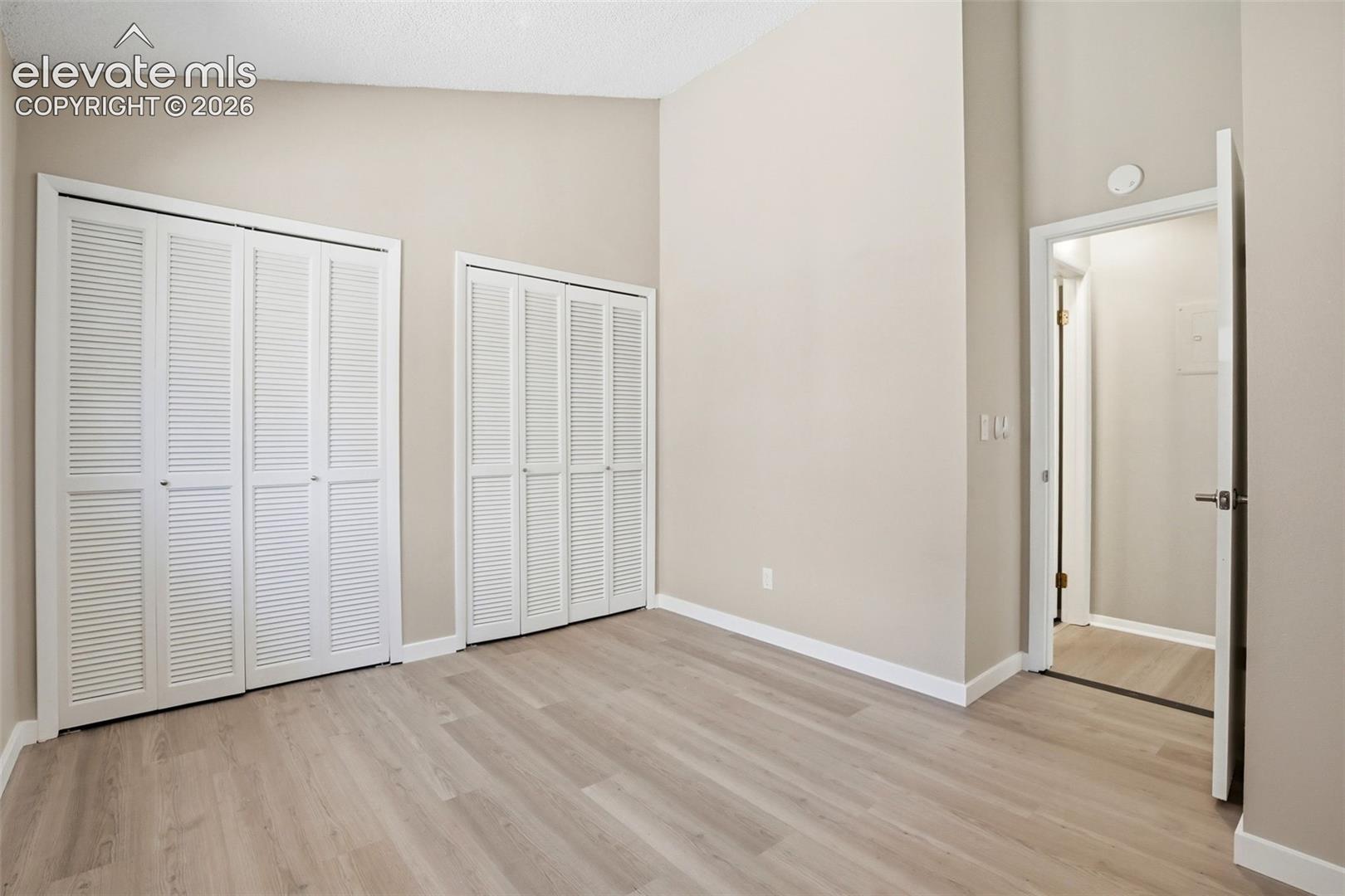 Spacious room featuring wood-finish flooring, neutral-toned walls, and a vaulted ceiling