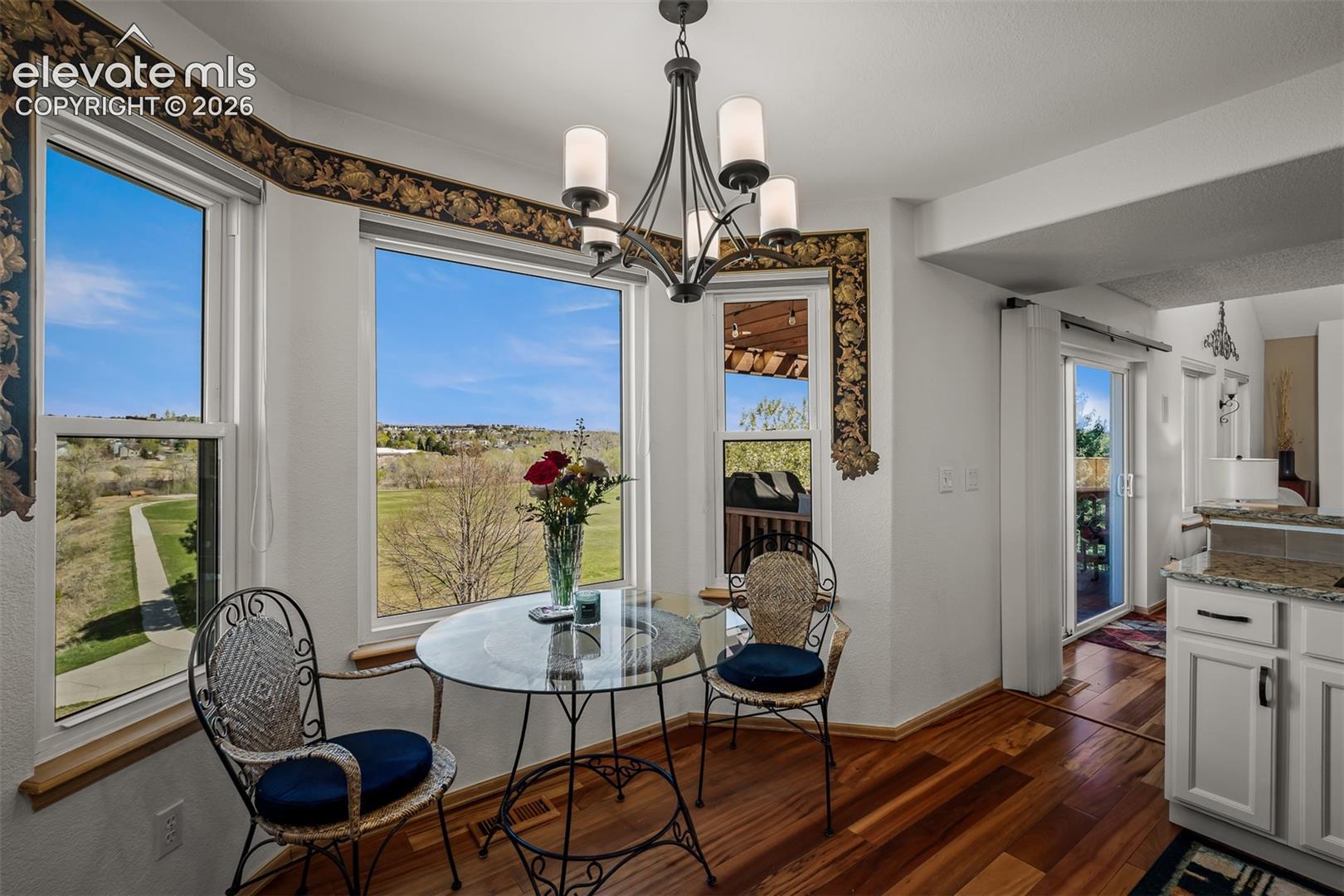 Breakfast area featuring expansive windows with landscape views of Cootonwood Park,  Brazilian Koa Hardwood flooring, a contemporary chandelier, and decorative wall trim.