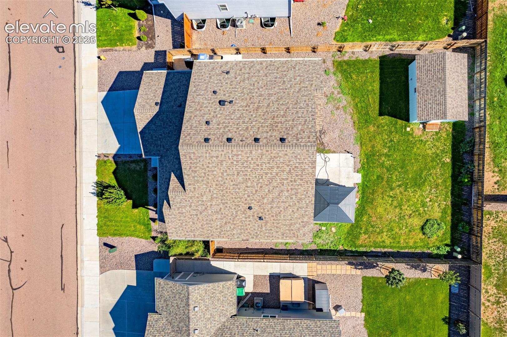 Paved driveway leading to a shingled roof property, featuring a fenced backyard with a lawn and an outdoor shed