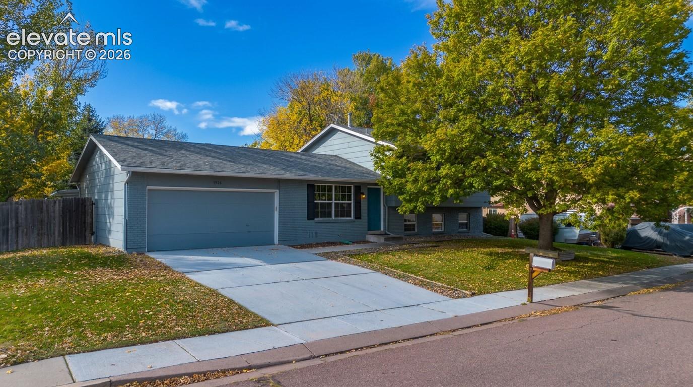 Split-level exterior featuring grey horizontal siding, asphalt shingle roofing, an attached two-car garage, concrete driveway, and mature trees