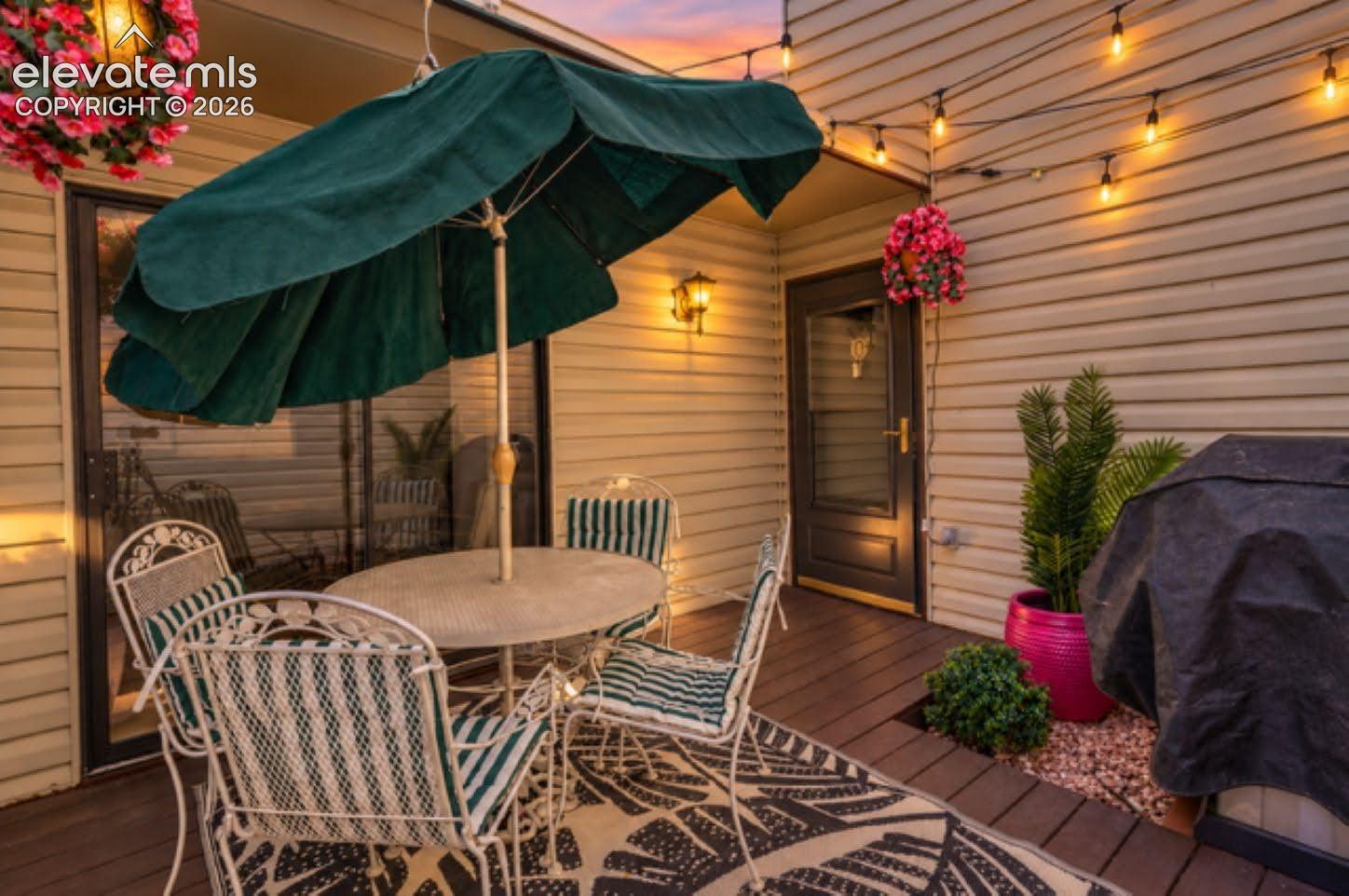Covered wood-plank deck featuring horizontal vinyl siding, a glass-paneled entry door, and wall-mounted exterior lighting