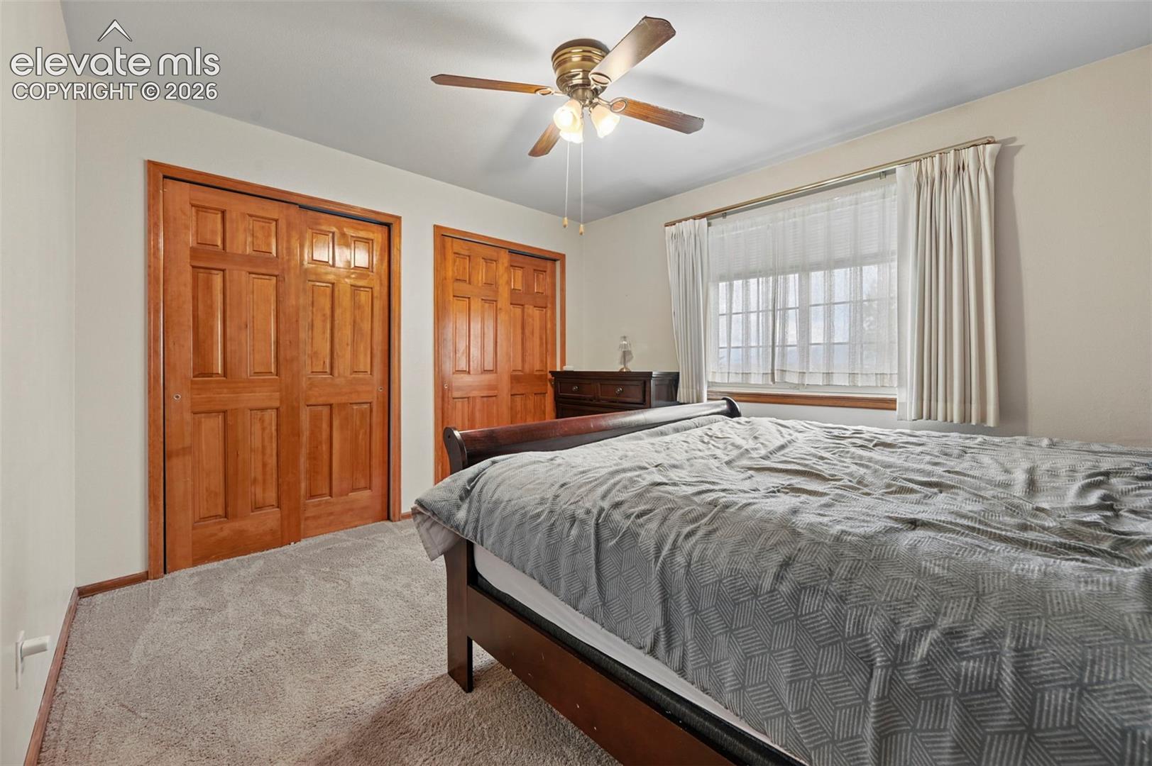 Second floor bedroom, warm-toned wood paneled closet doors, neutral wall paint, and a ceiling fan with integrated lighting