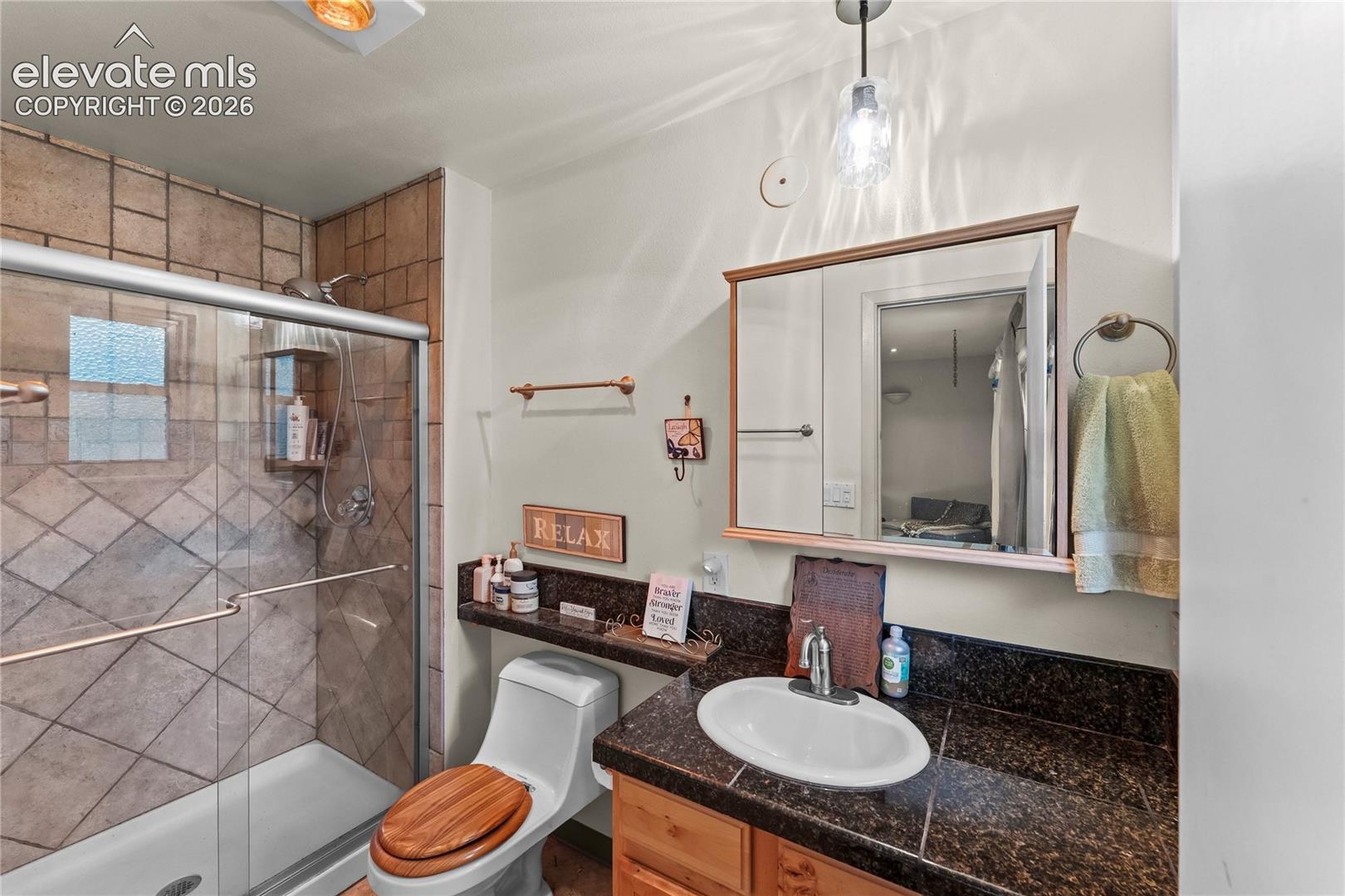 Bathroom featuring a glass-enclosed shower with tile surround, a built-in shower niche, a vanity with an integrated sink and dark countertop, a wood-framed medicine cabinet, and a wall-mounted light fixture