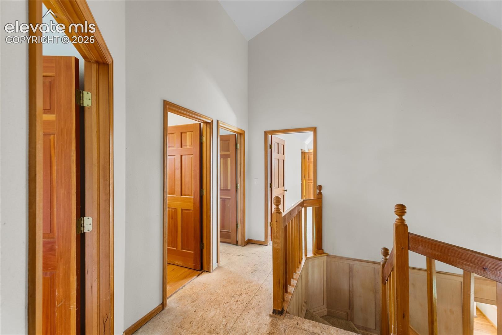 Vaulted ceiling, natural wood doors, wood staircase, wood railing, and light-toned walls