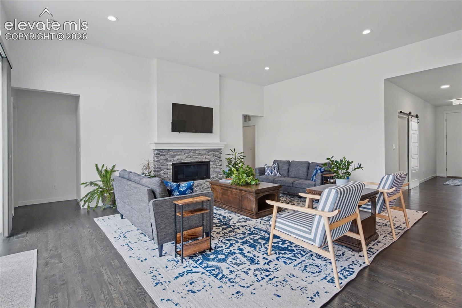 Living area featuring a barn door, recessed lighting, a stone fireplace, and dark wood finished floors