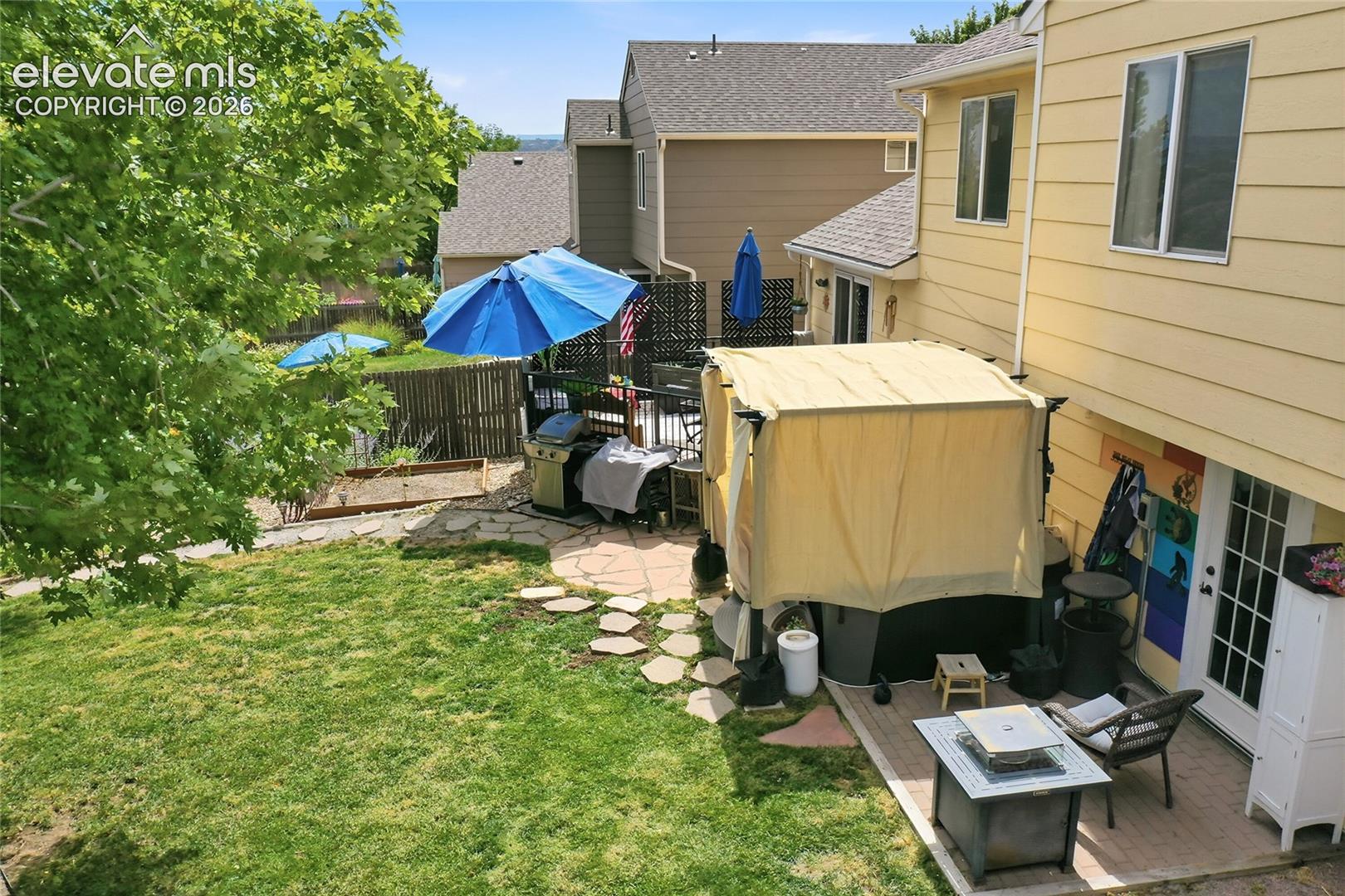 Backyard featuring a paved stone patio, irregular flagstone path, wood fence perimeter, and mature trees