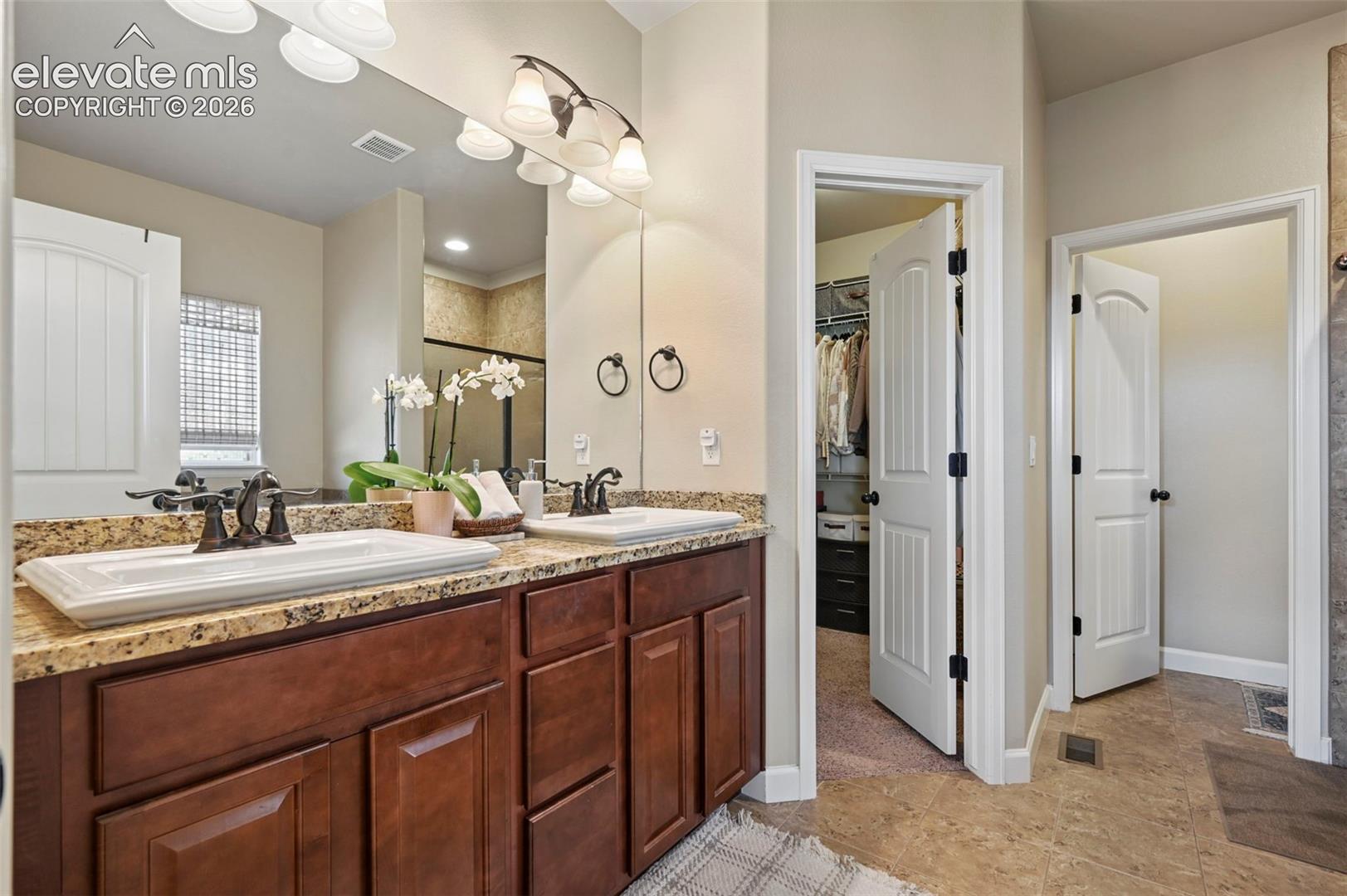 Dual vanities with stone-finish countertops, wood-finish cabinetry, and framed mirrors