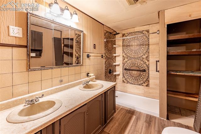 Bathroom featuring a stall shower, double vanity, wood finished floors, and tile walls