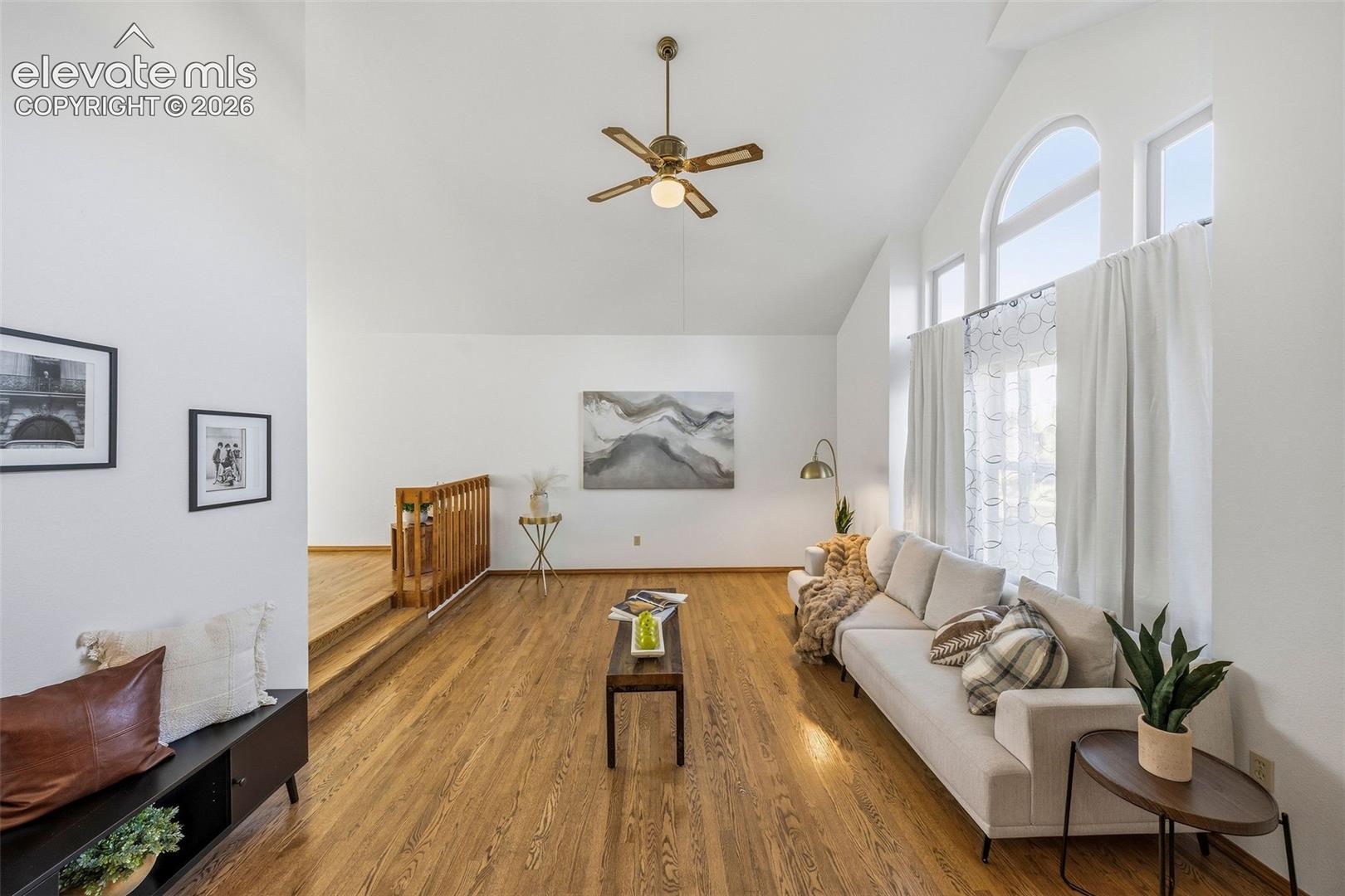 Vaulted ceilings, wood-finish flooring, architectural arch-top windows, and a multi-tiered floor plan featuring a wooden balustrade