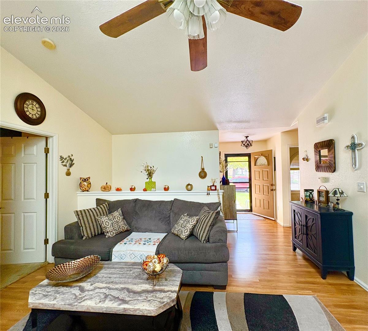 Vaulted ceiling with a ceiling fan, wood-finish flooring, two-panel interior door, and an exterior door with a decorative screen