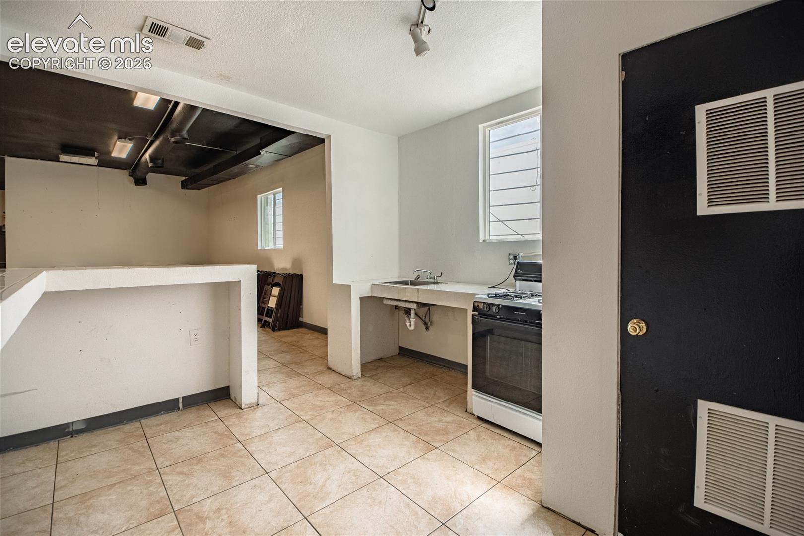 Tile flooring, exposed ceiling ducts, built-in counter, built-in sink, and a four-burner range