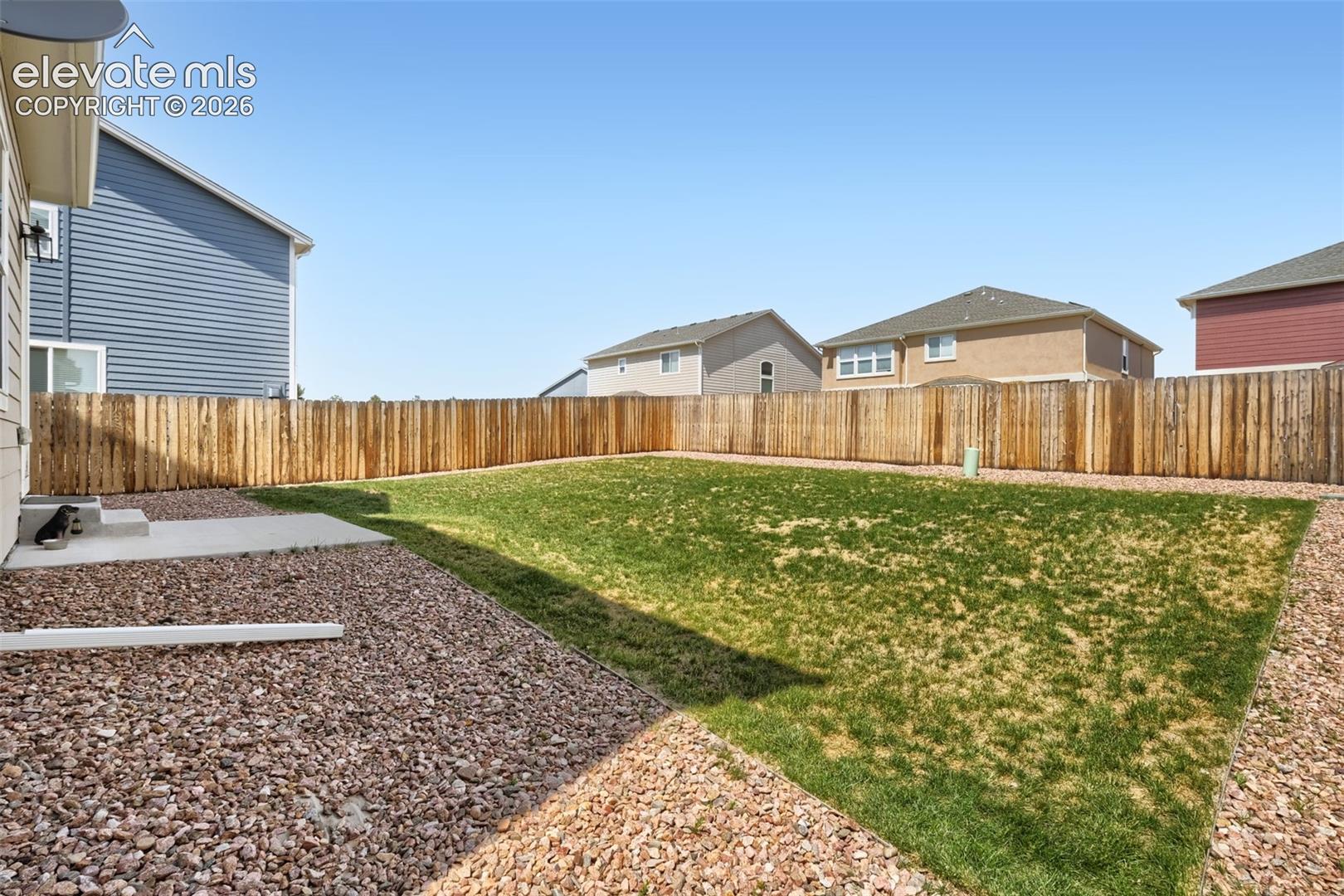 Fenced backyard featuring a large grass lawn, gravel landscaping, and a concrete patio pad
