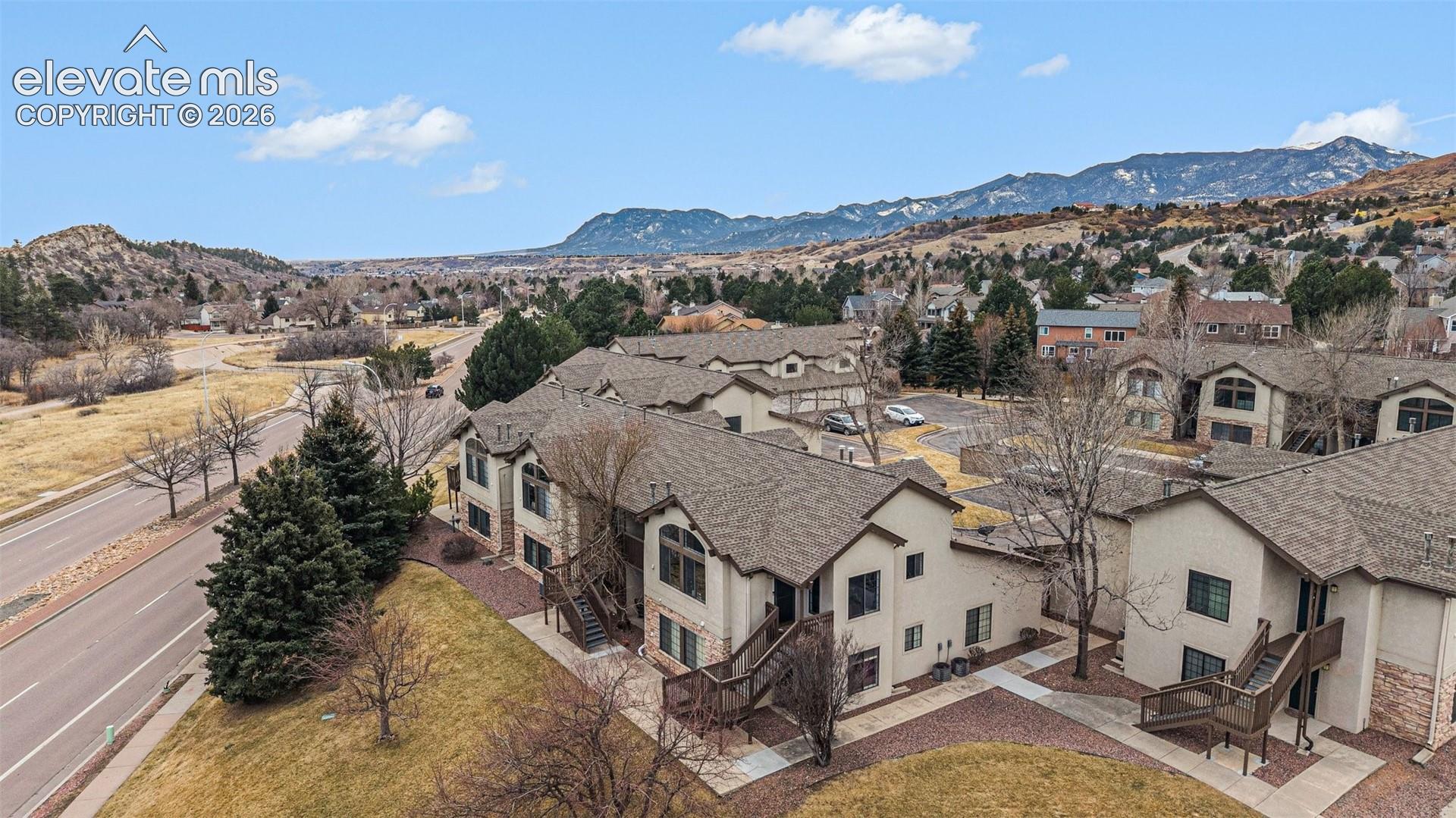 Multi-family residential complex featuring stucco siding, stone veneer accents, multi-gabled roofs, and elevated wooden balcony structures, set against a prominent mountain backdrop