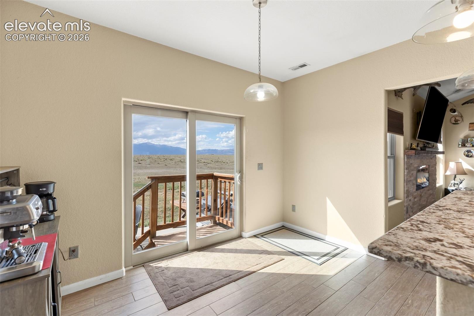 Sliding glass door opening to a wood deck, mountain landscape, hard-surface flooring, stone-veneer accent wall, and pendant lighting