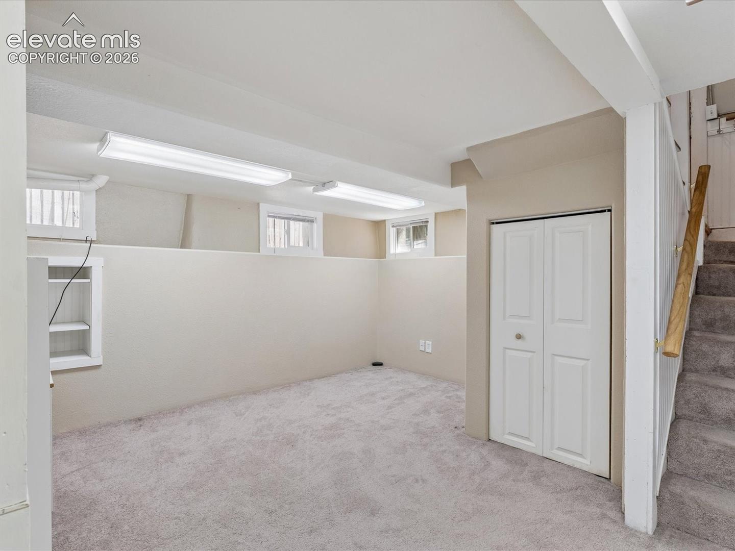 Carpeted room featuring multiple egress windows, built-in shelving, bi-fold closet doors, and recessed fluorescent lighting
