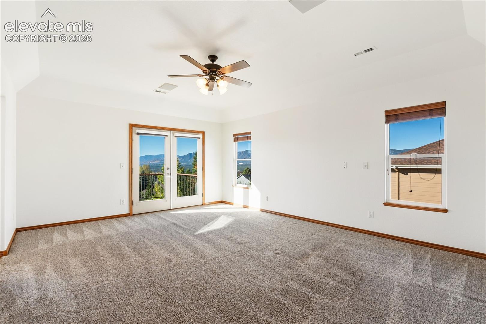 Tray ceiling with a central multi-blade ceiling fan, wall-to-wall carpeting, glass-paneled double doors, and windows featuring mountain scenery