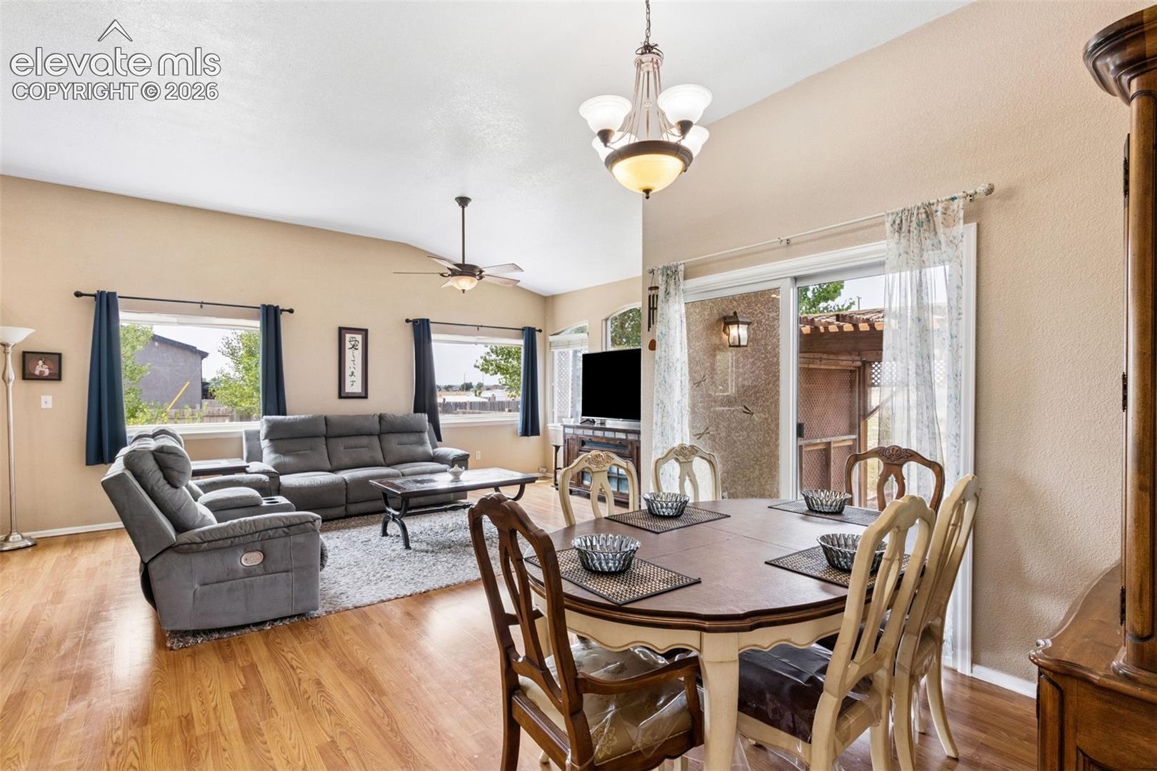 Vaulted ceilings featuring a multi-arm chandelier, wood-finish flooring, sliding glass patio door, and a ceiling fan