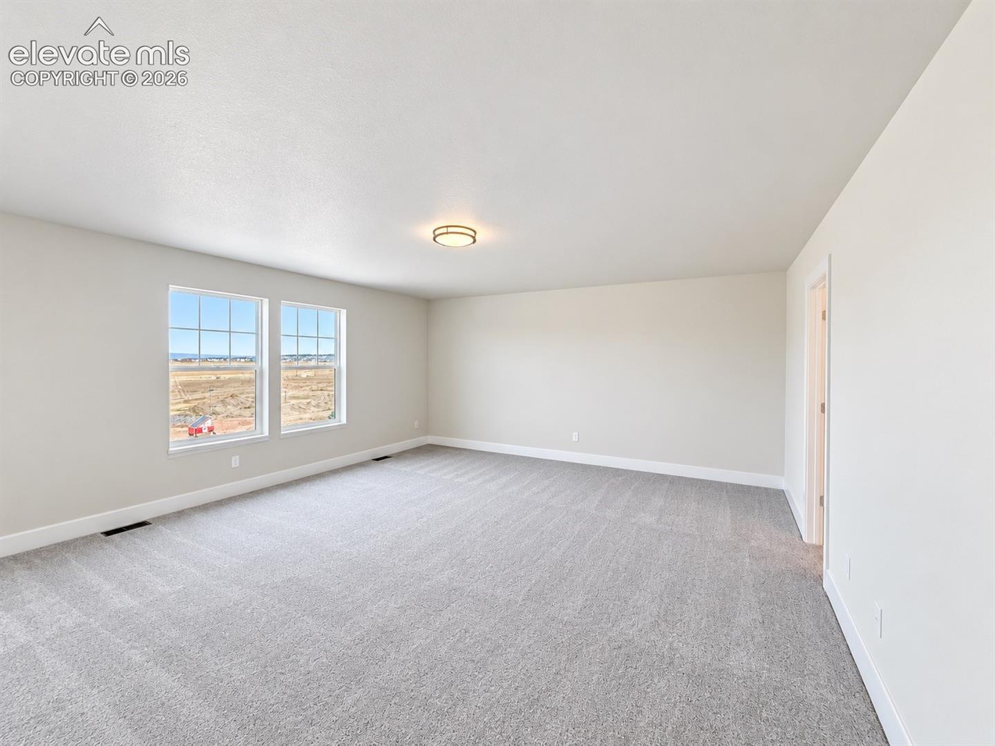 Interior space featuring neutral wall tones, wall-to-wall carpeting, dual grid-pattern windows, and a flush-mount circular ceiling fixture