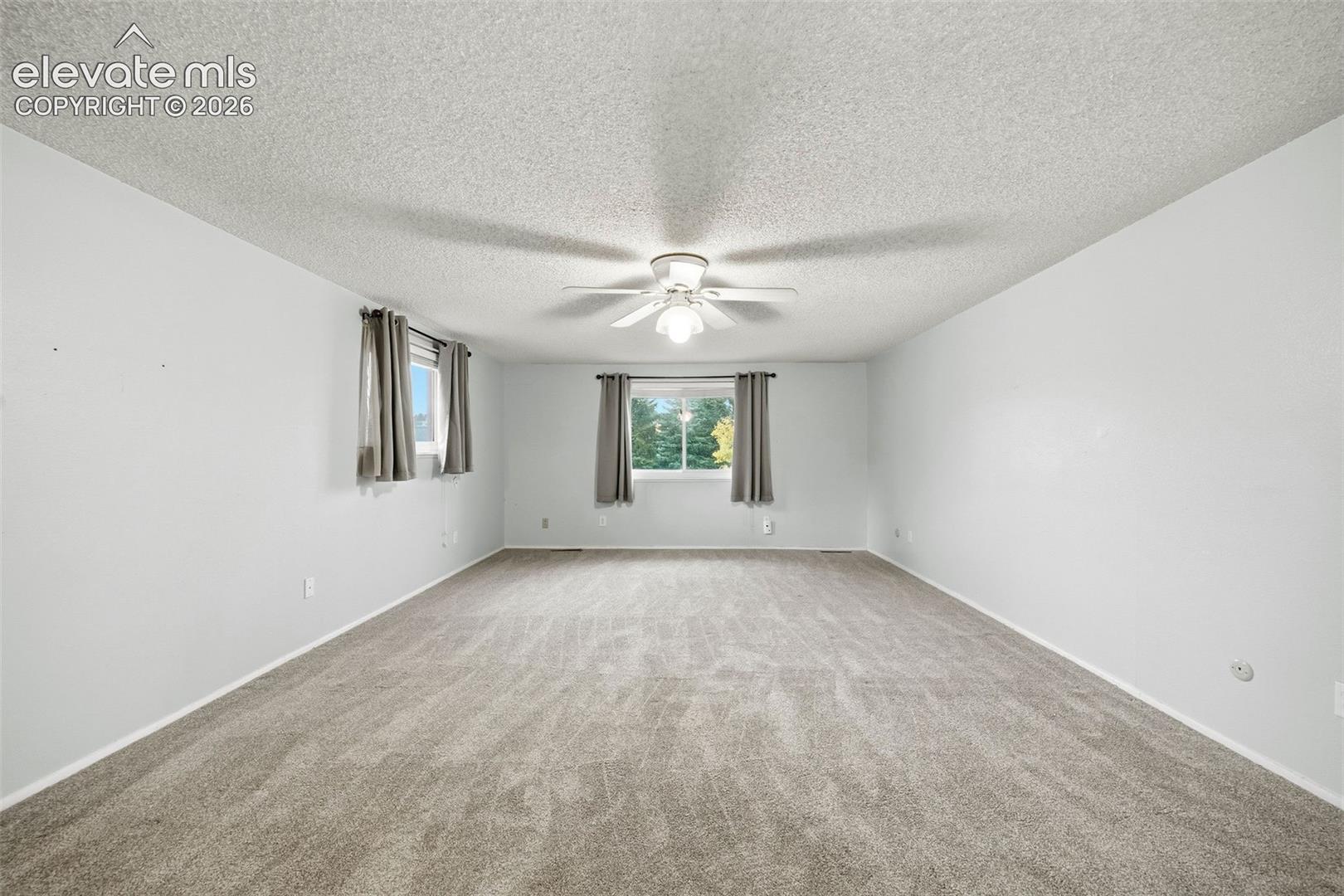 Neutral-toned wall-to-wall carpeting, textured ceiling, and center-mounted ceiling fan with integrated light fixture