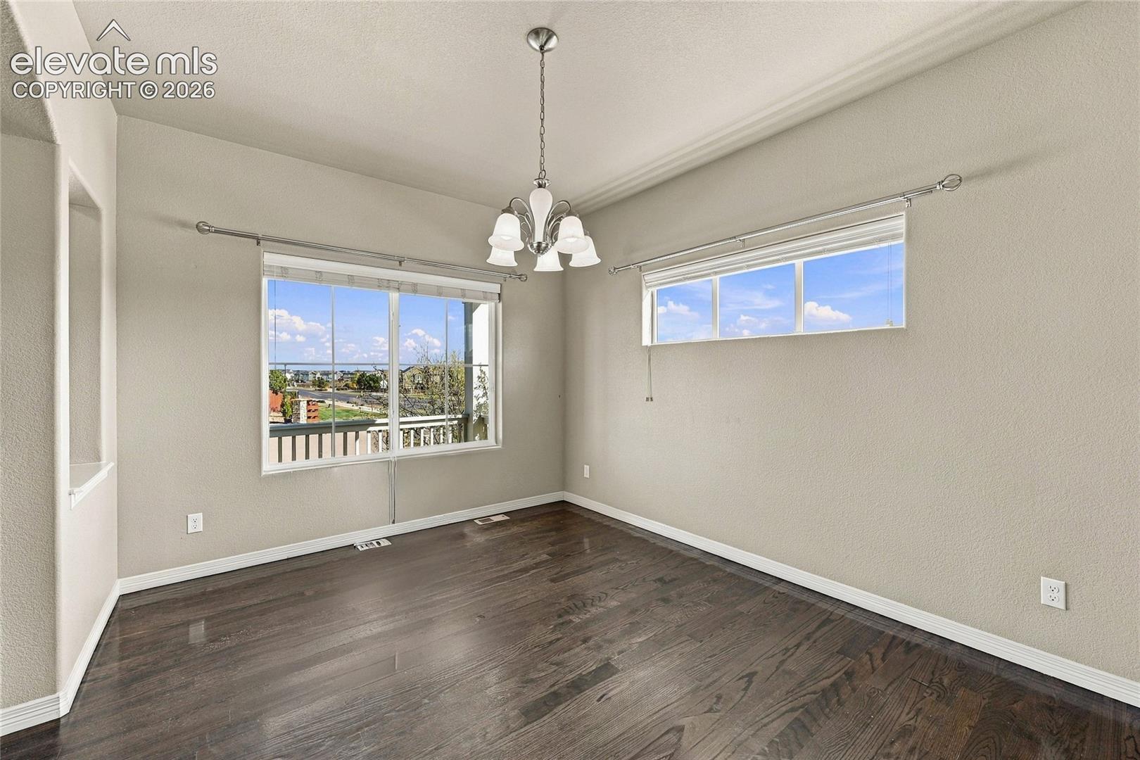 Interior space featuring wood-finish flooring, a multi-light metal chandelier, and dual windows with metal drapery hardware